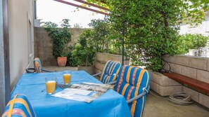 An outdoor patio with a table set for two, covered with a blue tablecloth, two striped chairs, and two glasses of orange juice. - Apartments Ana &amp; Bogdan - Two Bedroom Apartment With Terrace (Postira)
