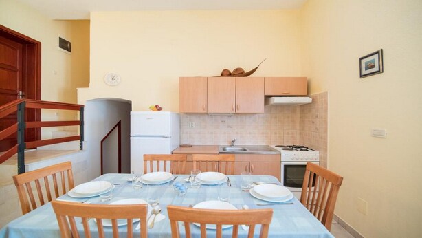 A compact kitchen with wooden cabinets, a white refrigerator, a stove, and a dining table set for four. - Apartments Ana &amp; Bogdan - Two Bedroom Apartment With Terrace (Postira)
