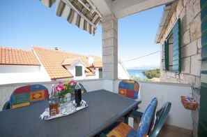 Ein Balkon mit einem für zwei Personen gedeckten Tisch, mit Blick auf eine Küstenlandschaft und traditionelle Gebäude.