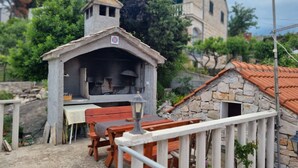 A rustic outdoor dining area with a stone-built structure, a wooden table, and benches. - Two Bedroom Apartment With Terrace (Supetar)