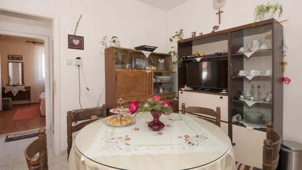 A dining area with a round table, chairs, a cabinet with dishes, and a television. - Two Bedroom Apartment With Terrace (Supetar)