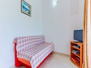 A room with a red sofa, a television on a wooden stand, and a bookshelf. - Apartments Ivo - One Bedroom Apartment With Terrace and sea View (Postira)