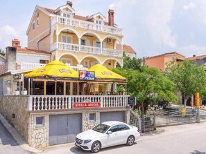 A two-story building with a balcony, a car parked in front, and a sign reading 'STELLA ARTOIS'. - Apartments Milic - Twin Room 1 - 2 (Obrovac)
