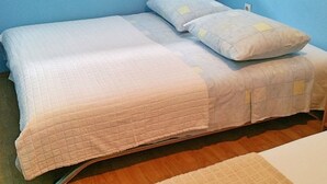 A single bed with a quilted bedspread and two pillows, a wooden floor, and a blue wall. - Apartments Mateo - One Bedroom Apartment - White (Vodice)