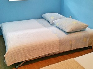A single bed with a quilted bedspread and two pillows, a wooden floor, and a blue wall. - Apartments Mateo - One Bedroom Apartment - White (Vodice)