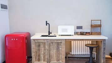 A compact kitchenette with a red refrigerator, a microwave, a sink, and a small bar stool.