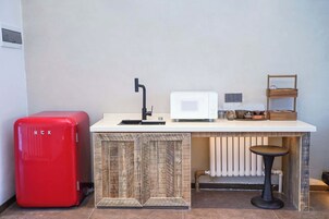 A compact kitchenette with a red refrigerator, a microwave, a sink, and a small bar stool.