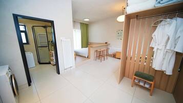 Et hotelværelse med seng, lille skrivebord, stol, radiator, tørrestativ og garderobeskab.