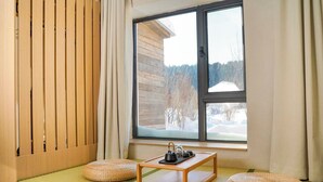 A room with tatami flooring, a wooden table with a tea set, and a window with a view of a snowy landscape. - FAYU-ecovillage (Yichun)