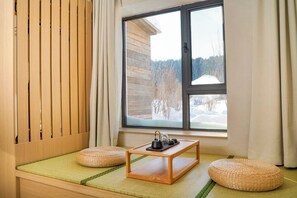 Une pièce au sol recouvert de tatamis, une table en bois avec un service à thé, et une fenêtre donnant sur un paysage enneigé.
