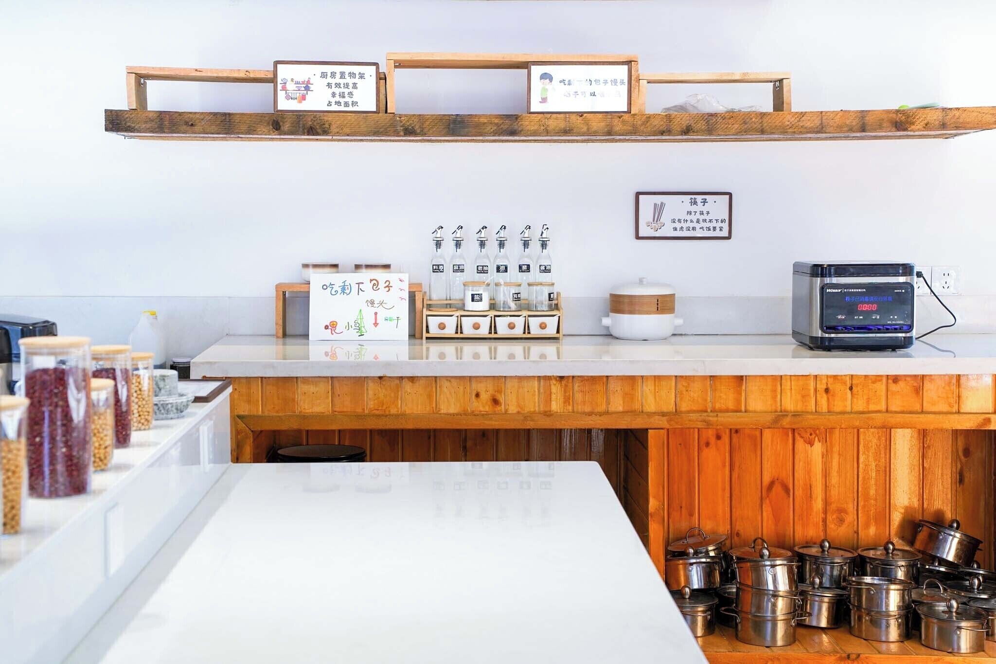 Una cocina con estantes de madera, frascos de especias, una olla arrocera y ollas de acero inoxidable.