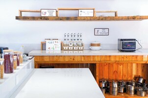 A kitchen area with wooden shelves, jars of spices, a rice cooker, and stainless steel pots.