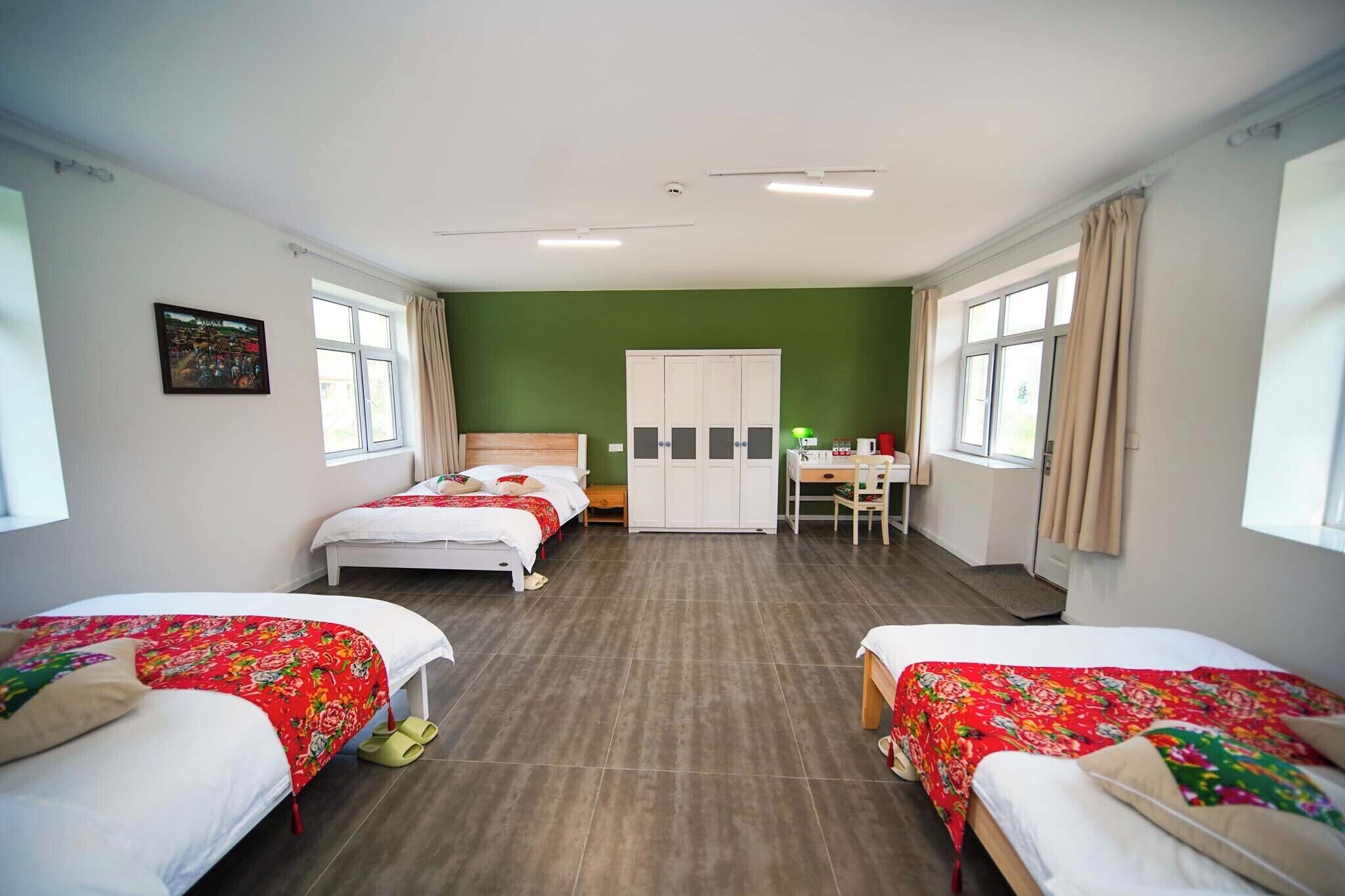 A hotel room with two beds, a desk, a wardrobe, and a green wall.