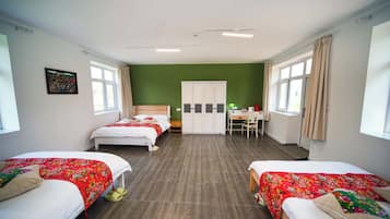 A hotel room with two beds, a desk, a wardrobe, and a green wall.