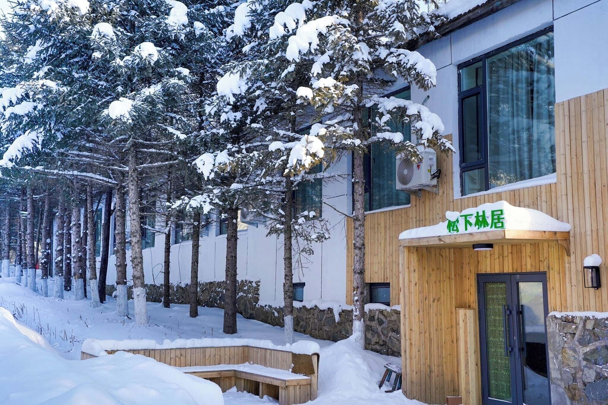A snow-covered building with a wooden facade, a stone wall, and a sign with Chinese characters.