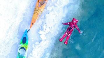 A kayaker in a red wetsuit and two kayaks on a frozen body of water.