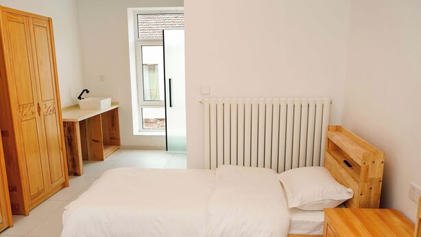 A bedroom with a bed, wooden wardrobe, bedside table, and a window with blinds. - FAYU-ecovillage (Yichun)