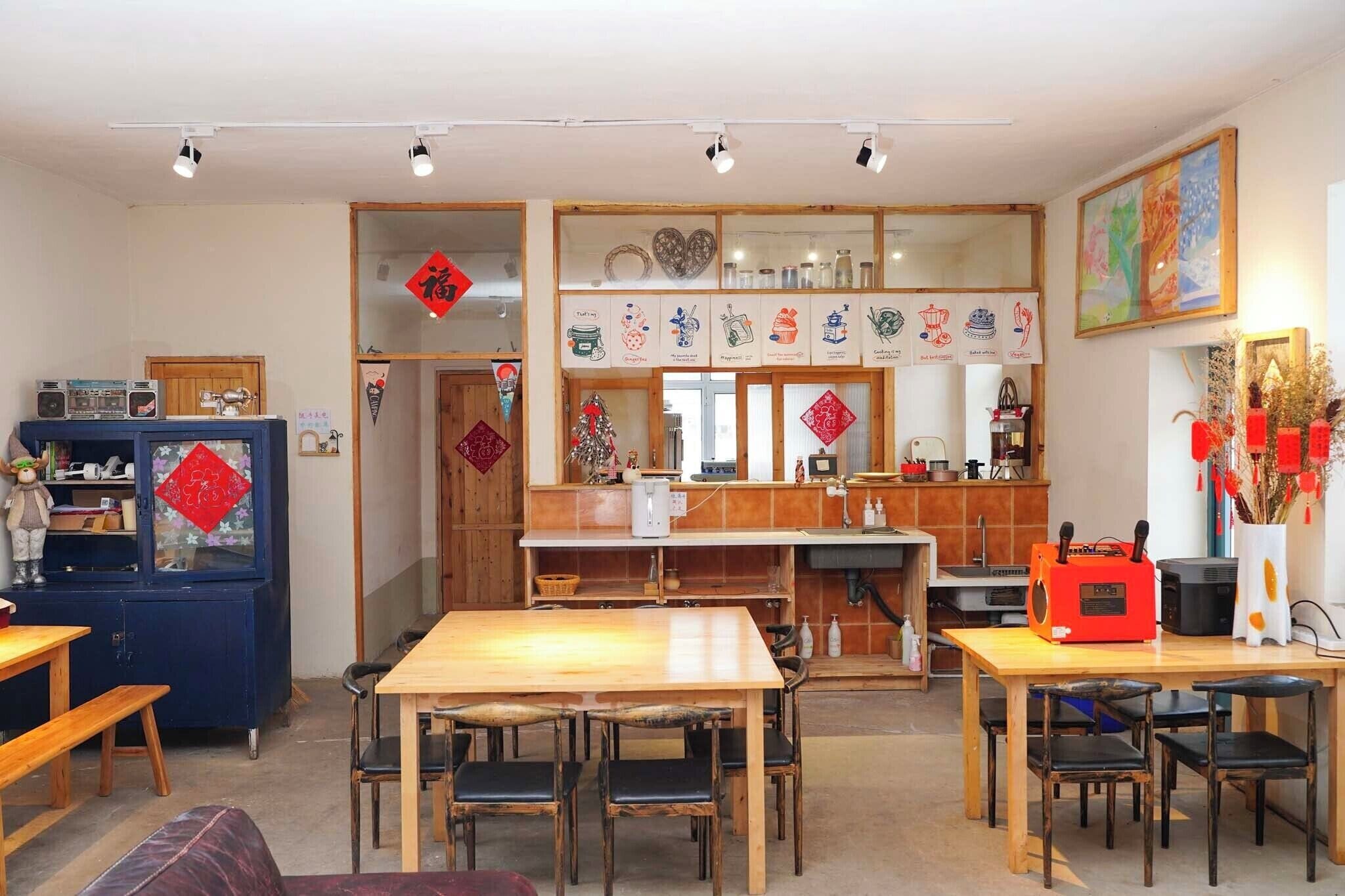 A dining area with a wooden table and chairs, a kitchen area with a sink and stove, and a decorative wall with hanging ornaments.