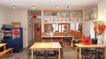 A dining area with a wooden table and chairs, a kitchen area with a sink and stove, and a decorative wall with hanging ornaments.