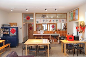 Un comedor con mesa y sillas de madera, una zona de cocina con pileta y cocina, y una pared decorativa con adornos colgantes.