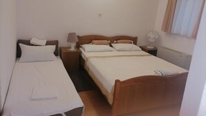 A standard hotel room with two single beds, a wooden headboard, a bedside table with a lamp, a wall-mounted fan, and a window with curtains. - Apartments Libertas - Studio With Balcony and Sea View - (Rogoznica)
