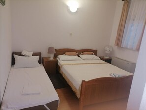 A standard hotel room with two single beds, a wooden headboard, a bedside table with a lamp, a wall-mounted fan, and a window with curtains. - Apartments Libertas - Studio With Balcony and Sea View - (Rogoznica)