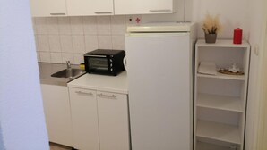 A compact kitchen with white cabinets, a black toaster oven, a white refrigerator, and a small shelf with decorative items. - Apartments Libertas - Studio With Balcony and Sea View - (Rogoznica)
