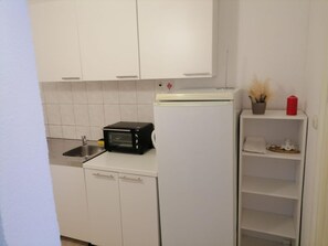 A compact kitchen with white cabinets, a black toaster oven, a white refrigerator, and a small shelf with decorative items. - Apartments Libertas - Studio With Balcony and Sea View - (Rogoznica)