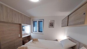 Ein Schlafzimmer mit zwei Betten, Holzwandverkleidung, einem Fenster mit Fensterläden und einem gerahmten Bild an der Wand.
