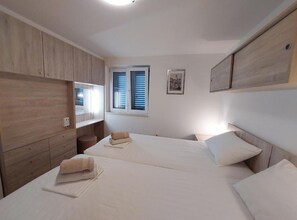Ein Schlafzimmer mit zwei Betten, Holzwandverkleidung, einem Fenster mit Fensterläden und einem gerahmten Bild an der Wand.