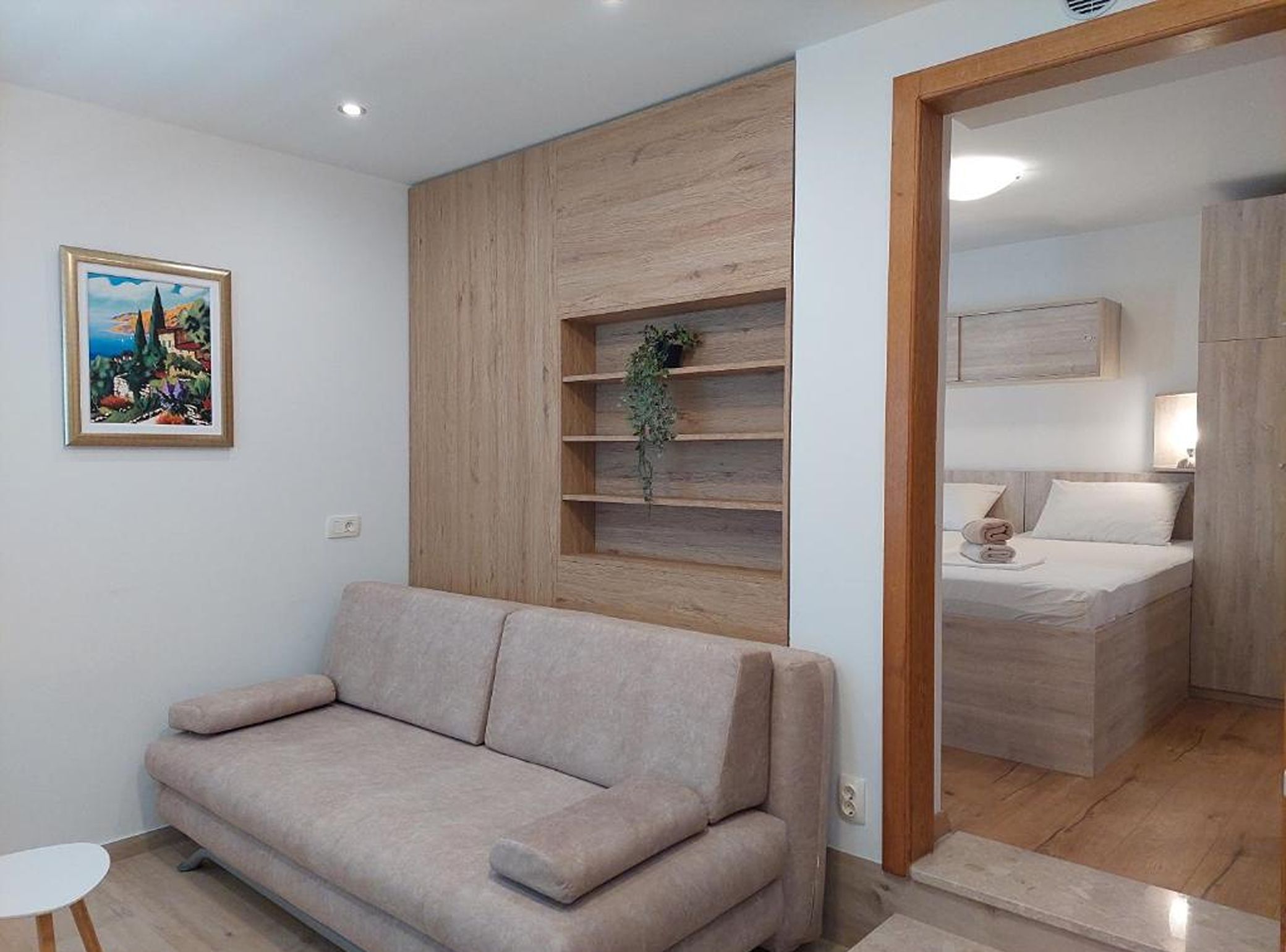 A modern living room with a beige sofa, a wooden accent wall, and a small plant.