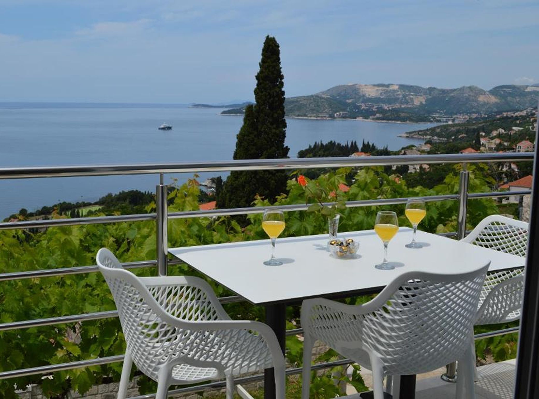 A table with chairs on a balcony overlooking a body of water and a distant landscape.