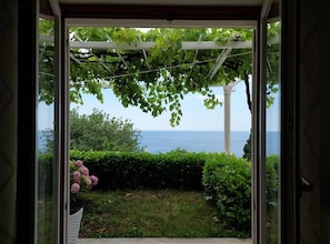 Vista a través de una puerta a un jardín con un pérgola, un seto y una masa de agua al fondo.