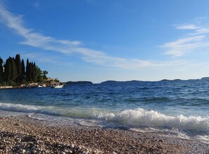 A pebble beach with clear blue water and distant hills. - Apartments Spilan (Zupa dubrovacka)