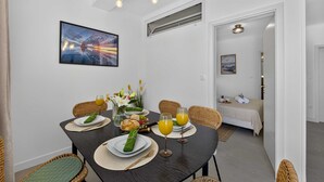 A dining area with a table set for two, a painting on the wall, and a view into a bedroom. - Sea Escape (Zupa dubrovacka)