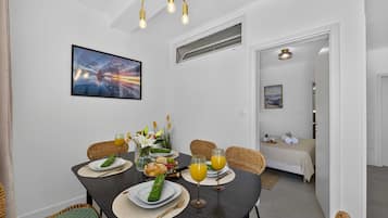 A dining area with a table set for two, a painting on the wall, and a view into a bedroom.