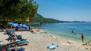 A beach with clear water, umbrellas, and beach chairs. - Sea Escape (Zupa dubrovacka)