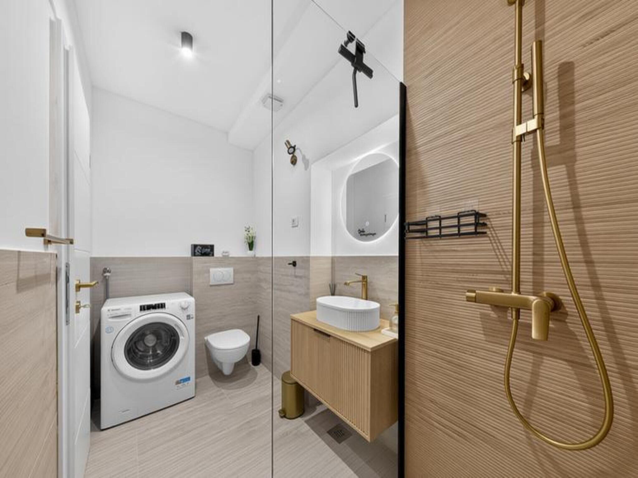 Uma casa de banho moderna com máquina de lavar roupa, sanita, lavatório e área de duche.