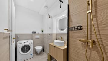 Uma casa de banho moderna com máquina de lavar roupa, sanita, lavatório e área de duche.