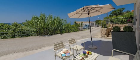 Una terraza con una mesa, sillas y un paraguas, con vistas a una carretera y vegetación.