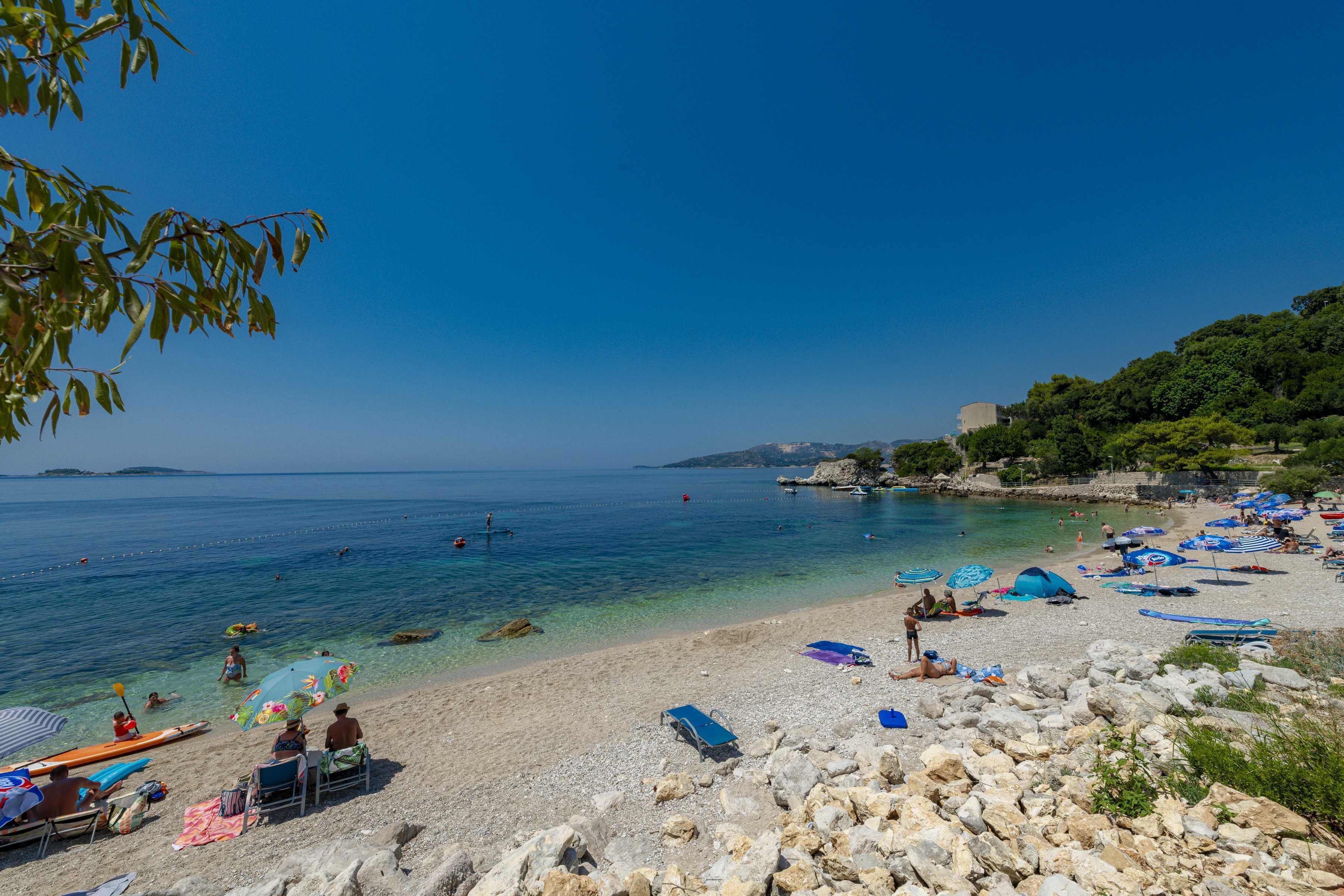 Una playa con aguas cristalinas, costa rocosa y sombrillas.