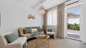 A modern living room with a sofa, armchair, and coffee table, a chandelier, and a sliding glass door to an outdoor area. - Sea Escape (Zupa dubrovacka)