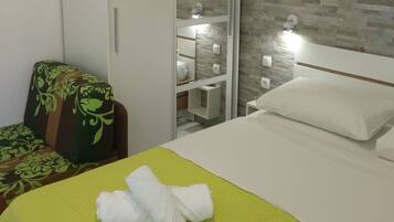 A hotel room with a bed, a chair, a wardrobe, and a mirror.