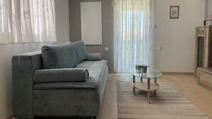A modern living room with a grey sofa, a glass coffee table, and a wooden cabinet. - Apartmani Meri (Vodice)