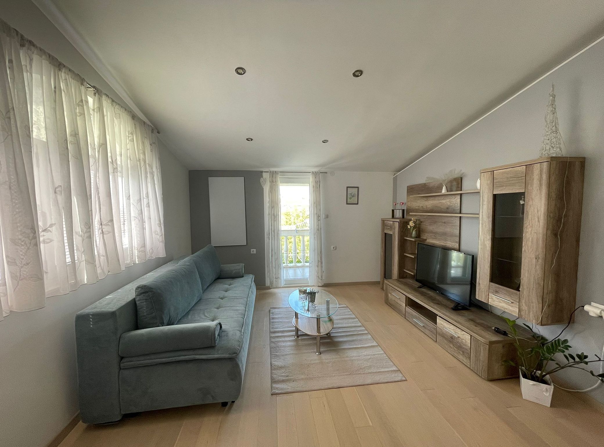Una sala de estar moderna con un sofá gris, una mesa de centro de vidrio y un mueble de entretenimiento de madera con un televisor.