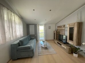 A modern living room with a grey sofa, a glass coffee table, and a wooden entertainment unit with a TV.
