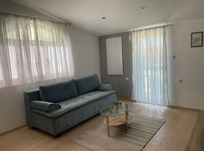 A modern living room with a grey sofa, a glass coffee table, and sheer curtains. - Apartmani Meri (Vodice)