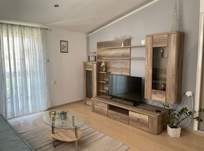 Un salón con mueble de madera para entretenimiento, una mesa de centro de vidrio y una planta en maceta.