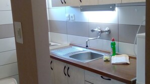 A kitchen with a stainless steel sink, a faucet, and a green bottle of dish soap on the counter. - Apartmani Meri (Vodice)