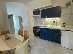 A modern kitchen with blue cabinets, a white countertop, and a dining area with a table and chairs. - Apartmani Meri (Vodice)